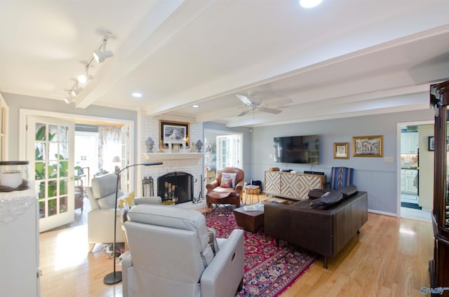 living room with a wealth of natural light, a fireplace, light wood-style floors, and beam ceiling