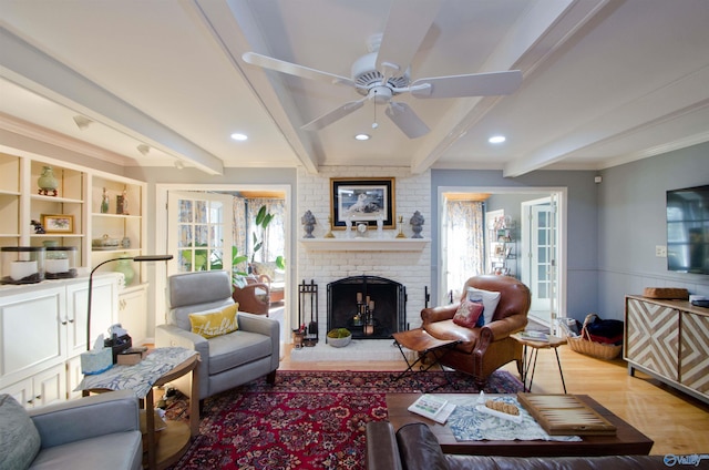 living area featuring a fireplace, a ceiling fan, crown molding, and beamed ceiling