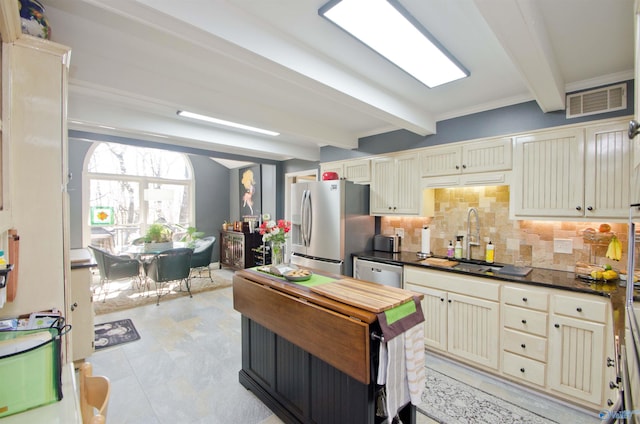 kitchen with stainless steel appliances, cream cabinets, dark countertops, beam ceiling, and visible vents