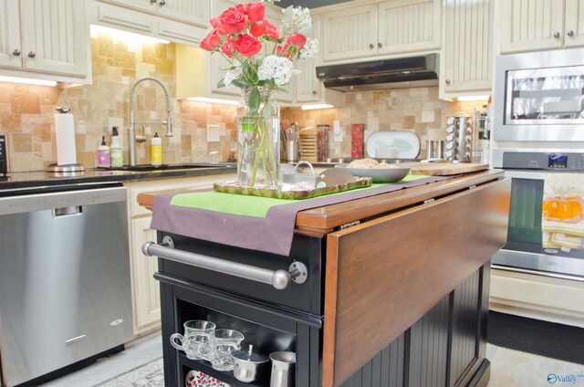 kitchen with stainless steel appliances, under cabinet range hood, decorative backsplash, cream cabinets, and a sink