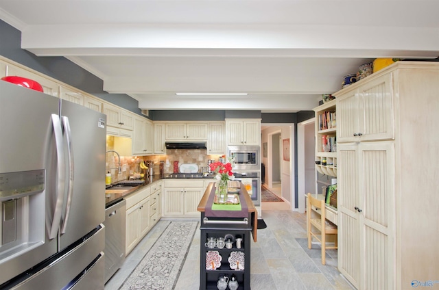kitchen featuring decorative backsplash, cream cabinetry, beam ceiling, appliances with stainless steel finishes, and a sink