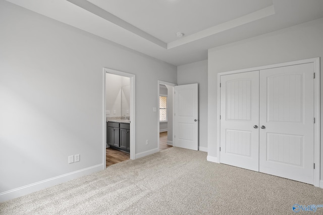 unfurnished bedroom featuring connected bathroom, a tray ceiling, a closet, and carpet floors