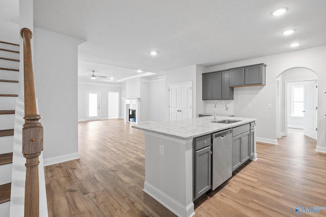 kitchen featuring a center island with sink, light stone countertops, stainless steel dishwasher, light wood-type flooring, and sink