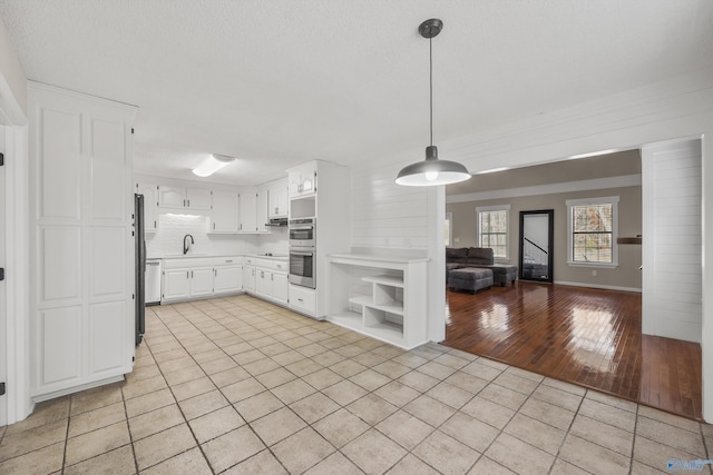 kitchen featuring light wood-type flooring, double oven, sink, pendant lighting, and white cabinets
