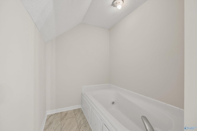 bathroom with a bathing tub, a textured ceiling, and vaulted ceiling