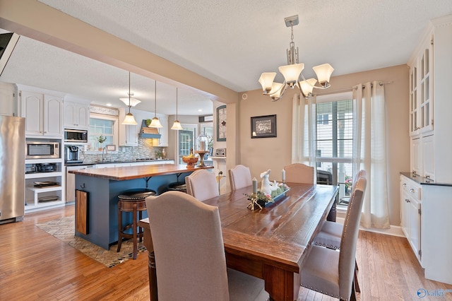 dining room featuring a textured ceiling, a notable chandelier, and light wood-style floors