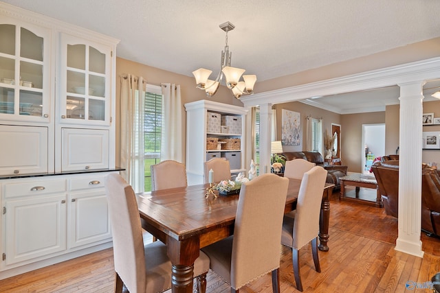 dining area featuring ornamental molding, decorative columns, light wood finished floors, and a notable chandelier