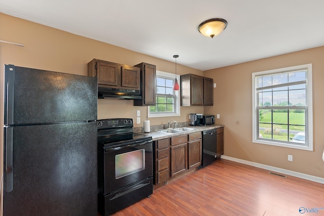 kitchen featuring visible vents, under cabinet range hood, a sink, light wood-style flooring, and black appliances