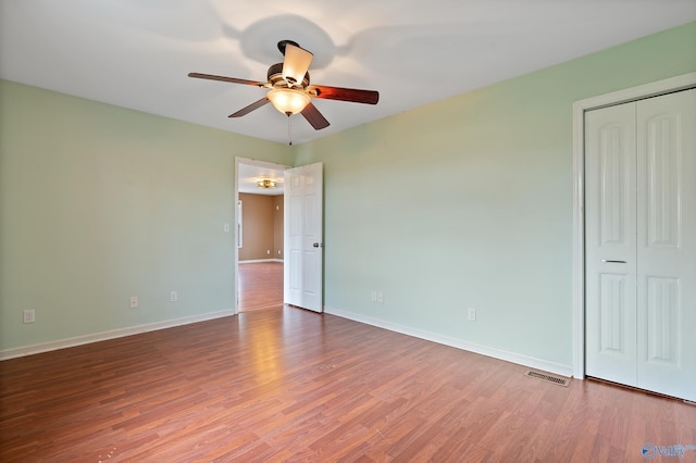 unfurnished bedroom with a ceiling fan, visible vents, wood finished floors, baseboards, and a closet