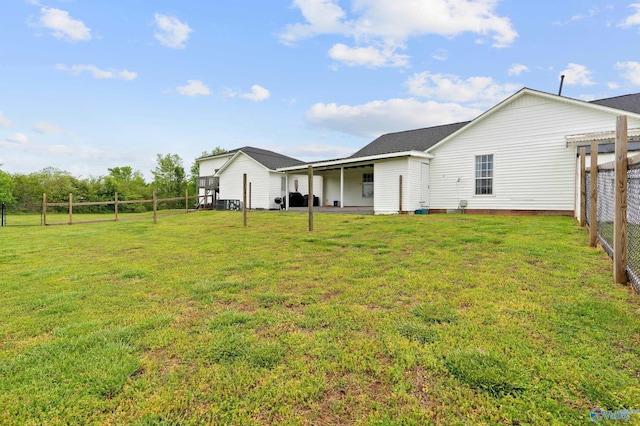 rear view of house with a lawn, a shingled roof, and fence