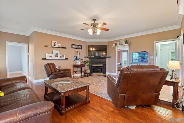 living area with ceiling fan, baseboards, a fireplace with flush hearth, wood finished floors, and ornamental molding