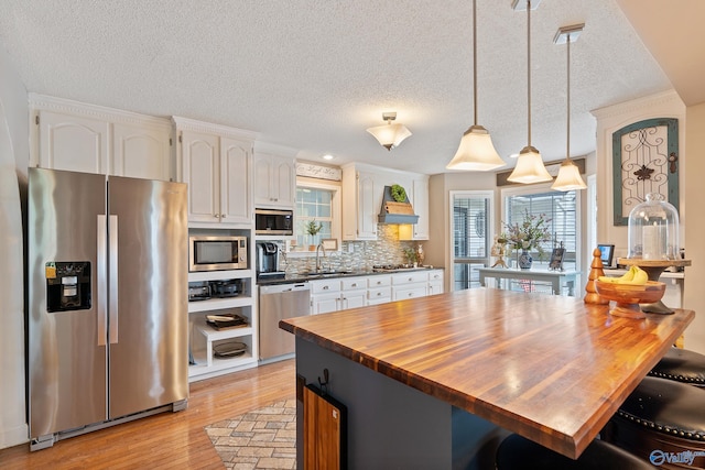 kitchen with white cabinets, custom range hood, light wood-style flooring, appliances with stainless steel finishes, and wood counters