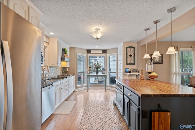 kitchen with white cabinetry, a textured ceiling, appliances with stainless steel finishes, and butcher block counters