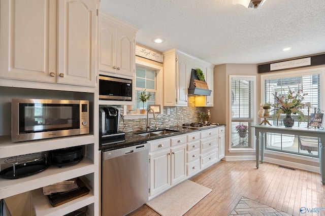 kitchen with a textured ceiling, visible vents, a sink, custom exhaust hood, and stainless steel appliances
