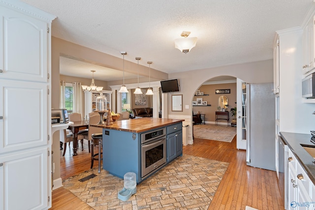 kitchen with butcher block countertops, light wood-style floors, white cabinetry, arched walkways, and stainless steel appliances