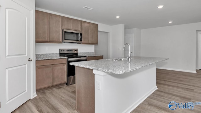 kitchen with stainless steel appliances, a kitchen island with sink, sink, and light hardwood / wood-style flooring