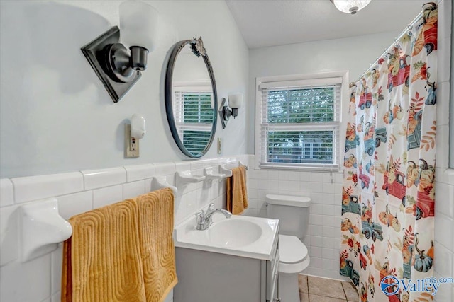 bathroom with tile patterned floors, toilet, tile walls, wainscoting, and vanity