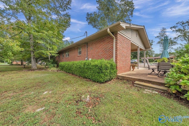 view of side of home featuring brick siding, a patio area, and a yard