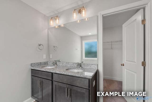 bathroom featuring double vanity, a spacious closet, baseboards, and a sink