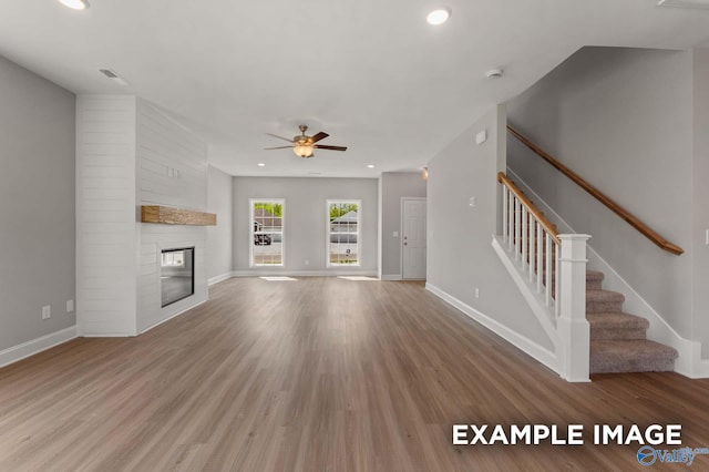 unfurnished living room featuring a large fireplace, baseboards, and wood finished floors