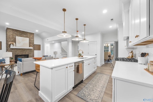 kitchen with appliances with stainless steel finishes, white cabinetry, sink, a fireplace, and decorative light fixtures