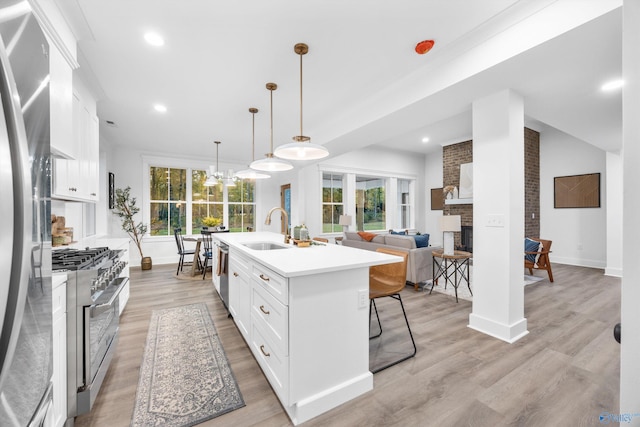 kitchen with a center island with sink, appliances with stainless steel finishes, white cabinetry, a wealth of natural light, and decorative light fixtures