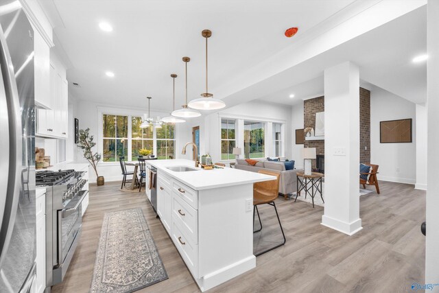 kitchen with a fireplace, white cabinets, light wood-style floors, stainless steel appliances, and an island with sink