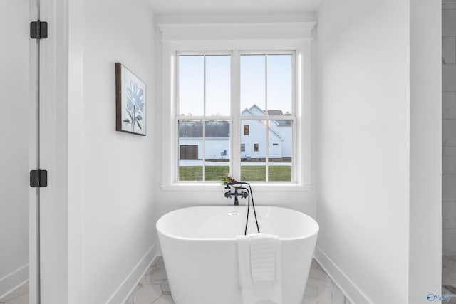 bathroom with baseboards, a freestanding tub, and marble finish floor