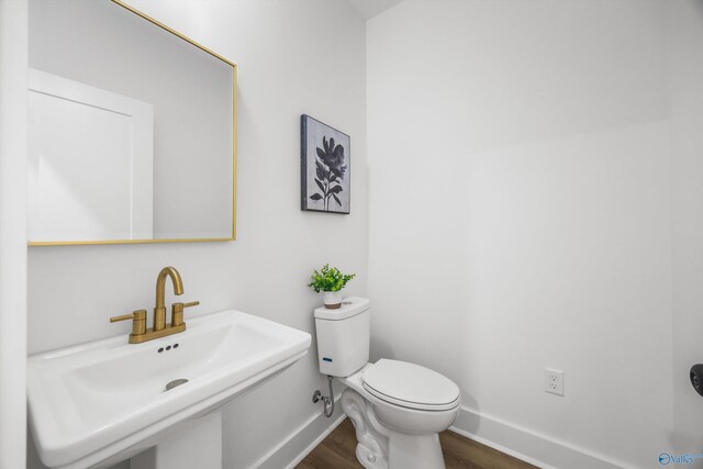 half bathroom with baseboards, a sink, wood finished floors, and toilet