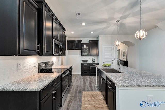 kitchen featuring arched walkways, decorative light fixtures, stainless steel appliances, a sink, and dark cabinets