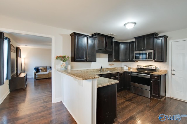 kitchen featuring dark wood-type flooring, appliances with stainless steel finishes, light stone countertops, and kitchen peninsula