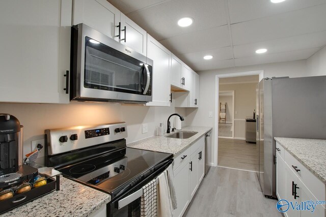 kitchen with light hardwood / wood-style floors, stainless steel appliances, sink, light stone counters, and white cabinets