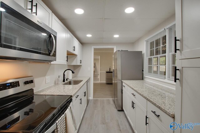 kitchen featuring stainless steel appliances, light stone counters, sink, white cabinets, and light hardwood / wood-style floors