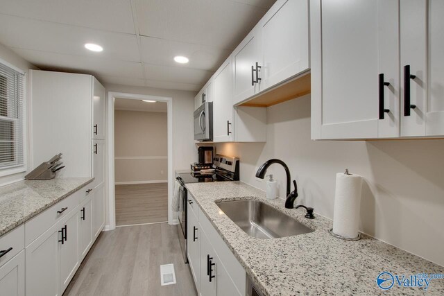 kitchen with light hardwood / wood-style flooring, appliances with stainless steel finishes, light stone counters, white cabinetry, and sink