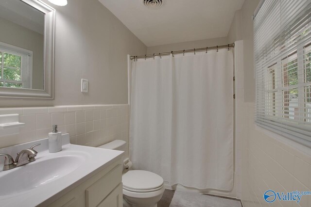 bathroom with toilet, vanity, tasteful backsplash, curtained shower, and tile walls