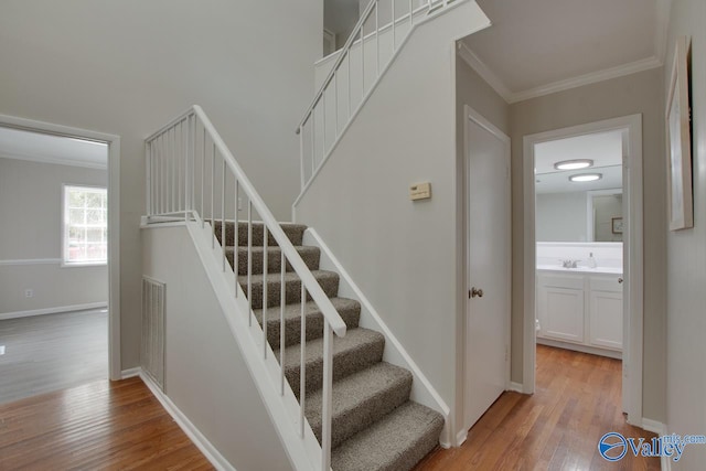 staircase featuring wood-type flooring, crown molding, and sink