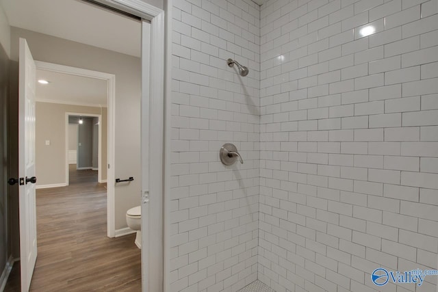 bathroom featuring wood-type flooring, ornamental molding, toilet, and tiled shower