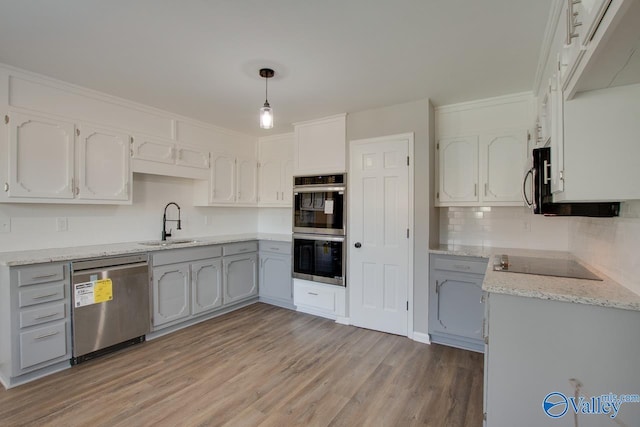 kitchen featuring appliances with stainless steel finishes, decorative light fixtures, sink, light hardwood / wood-style floors, and light stone countertops