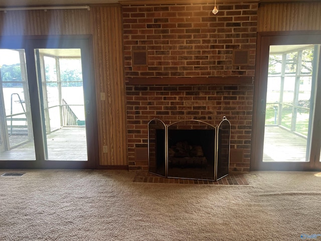 unfurnished living room with carpet flooring, visible vents, a fireplace, and a healthy amount of sunlight