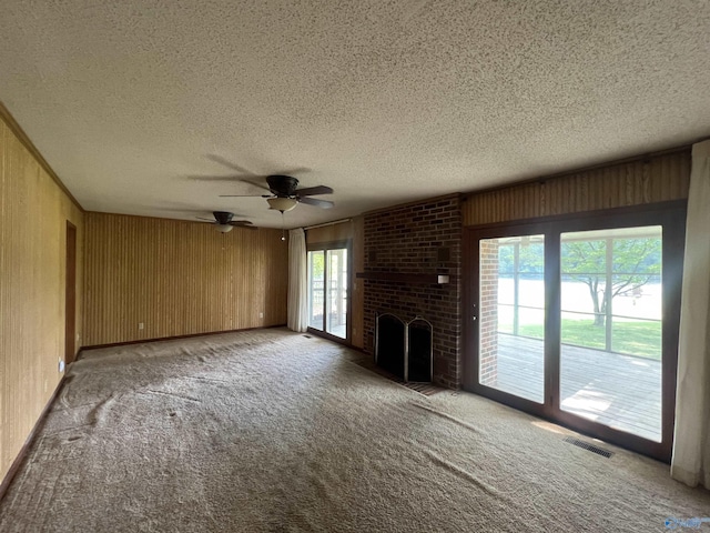 unfurnished living room featuring carpet floors, a textured ceiling, visible vents, wood walls, and ceiling fan