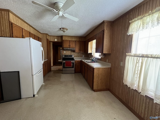 kitchen featuring a sink, stainless steel electric stove, brown cabinets, freestanding refrigerator, and light countertops