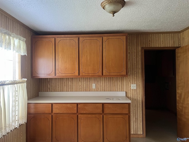 kitchen with brown cabinets, light countertops, wood walls, and a textured ceiling