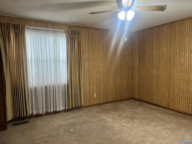 carpeted empty room with ceiling fan, a textured ceiling, visible vents, and wood walls