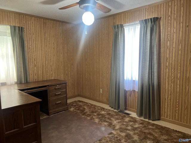 unfurnished office with a ceiling fan, a textured ceiling, dark colored carpet, visible vents, and wood walls