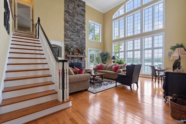 living room featuring a high ceiling, ornamental molding, a stone fireplace, and light wood-type flooring