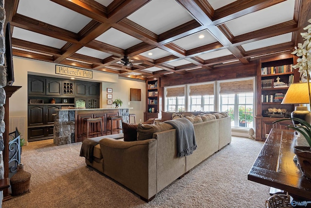 living room featuring built in shelves, beam ceiling, coffered ceiling, ceiling fan, and light colored carpet