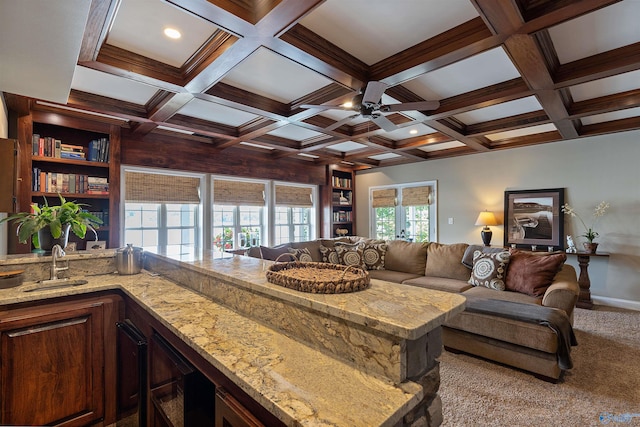 interior space with beamed ceiling, light stone counters, coffered ceiling, ceiling fan, and light colored carpet