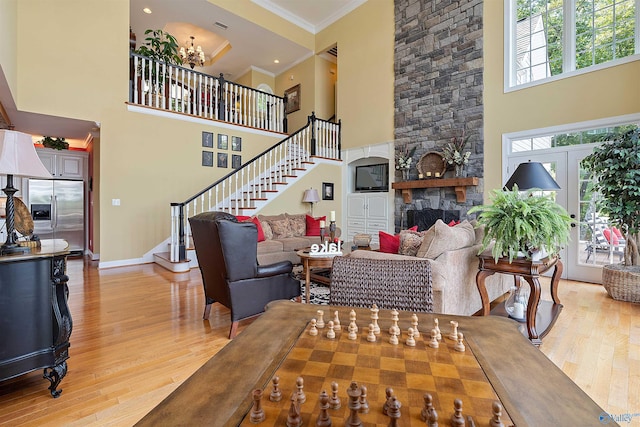 living room with light wood-type flooring, ornamental molding, a high ceiling, and a stone fireplace