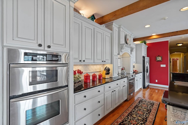 kitchen featuring beam ceiling, light hardwood / wood-style flooring, decorative backsplash, stainless steel appliances, and white cabinets