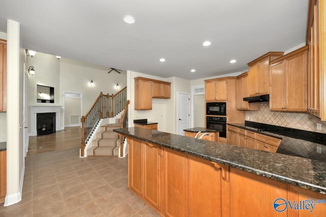 118 Conservancy Dr, Madison, AL 35758 - kitchen featuring black appliances, dark stone countertops, under cabinet range hood, tasteful backsplash, and a fireplace